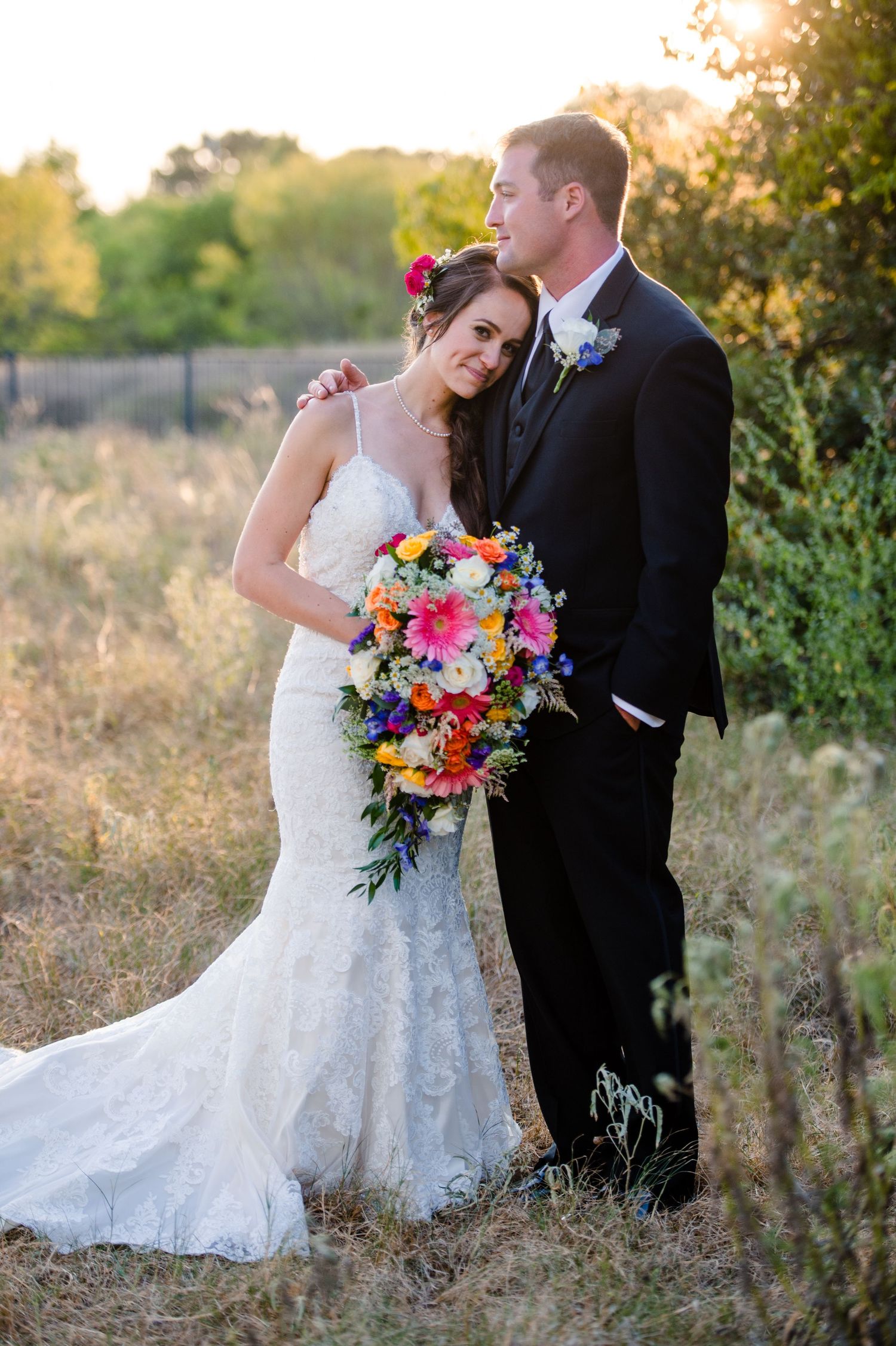 A romantic outdoor wedding photoshoot featuring a bride in a lace gown and groom in black suit during golden hour.