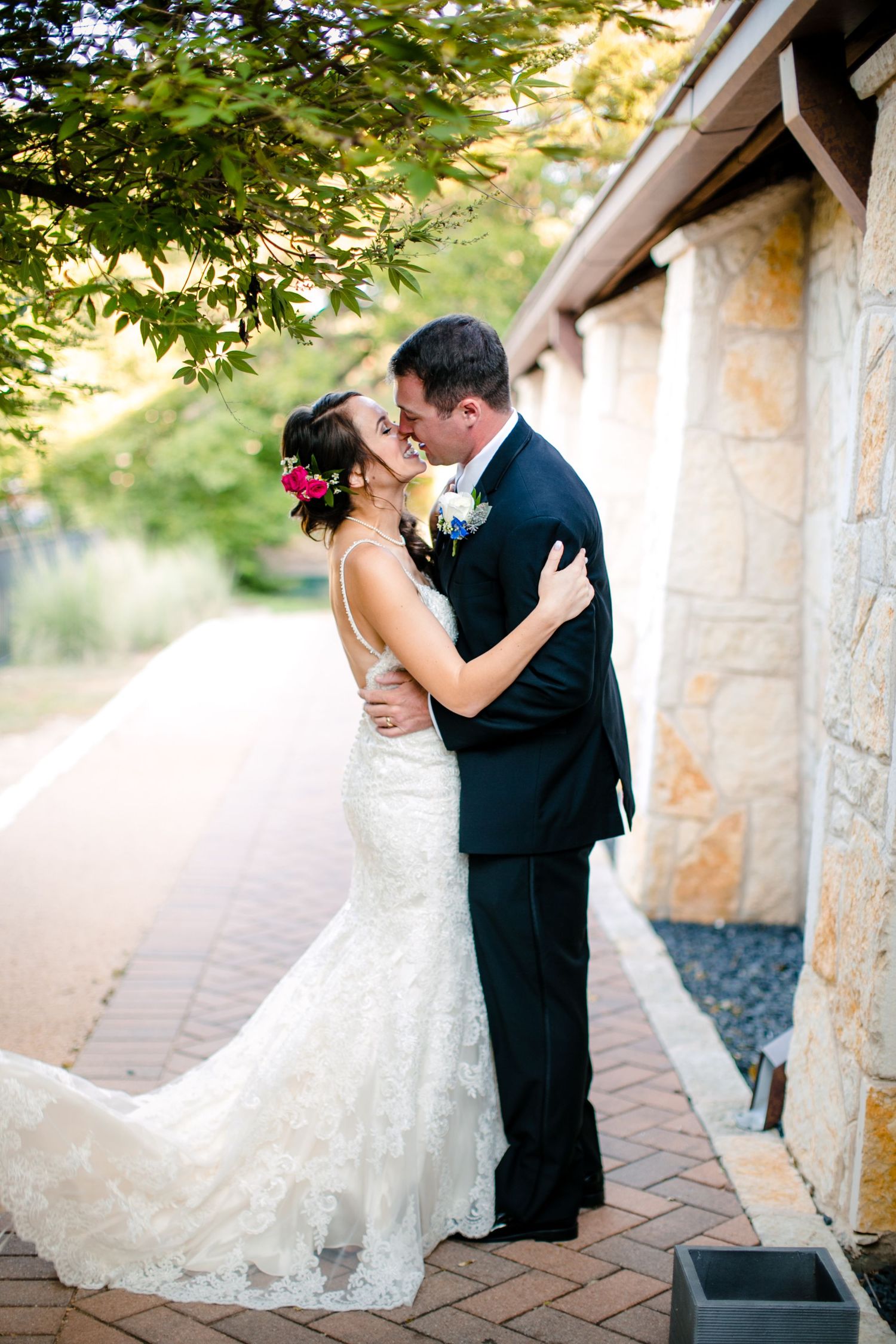 Romantic wedding couple embraces in an outdoor stone archway during golden hour.
