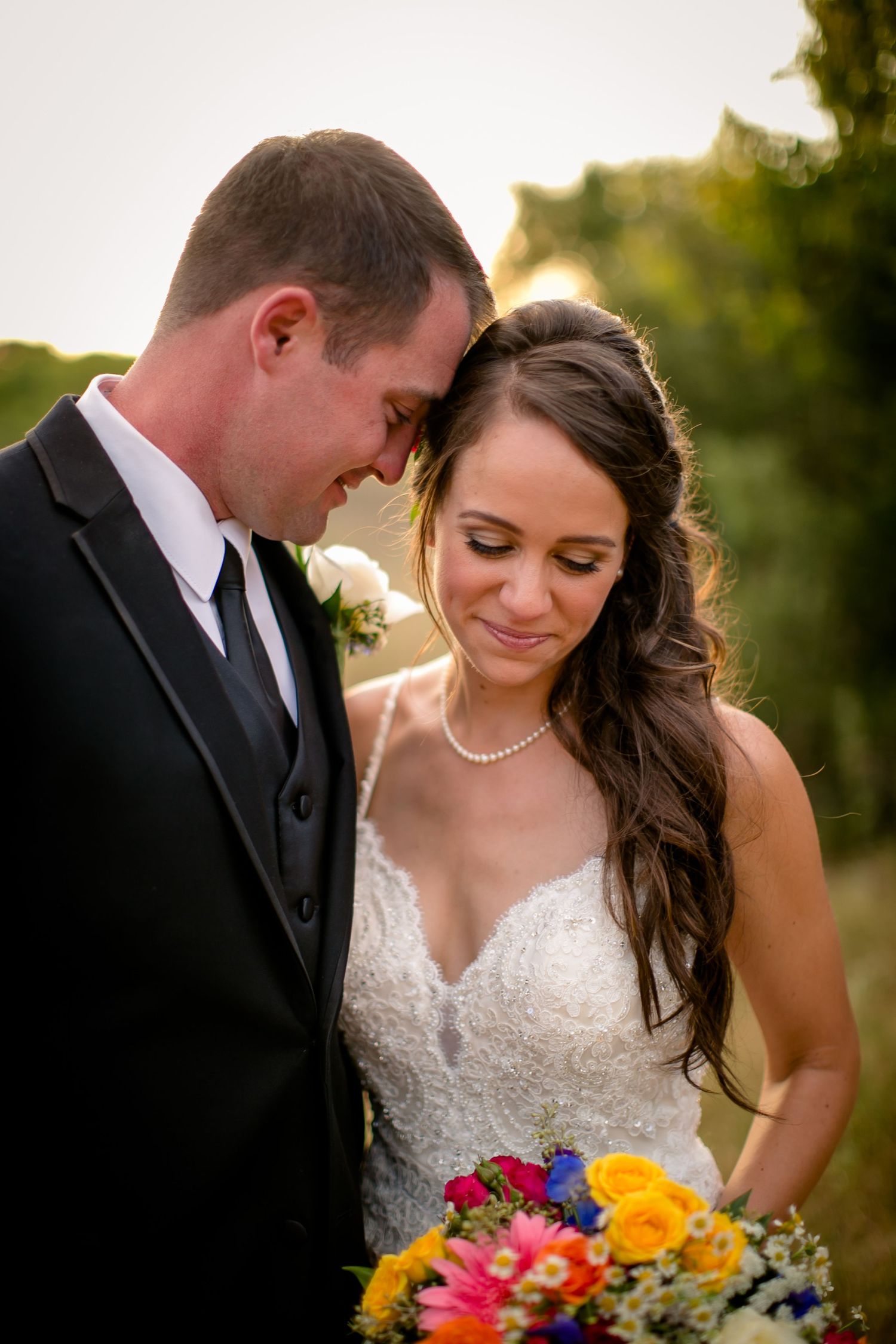 Wedding couple shares an intimate moment with colorful bouquet during sunset.