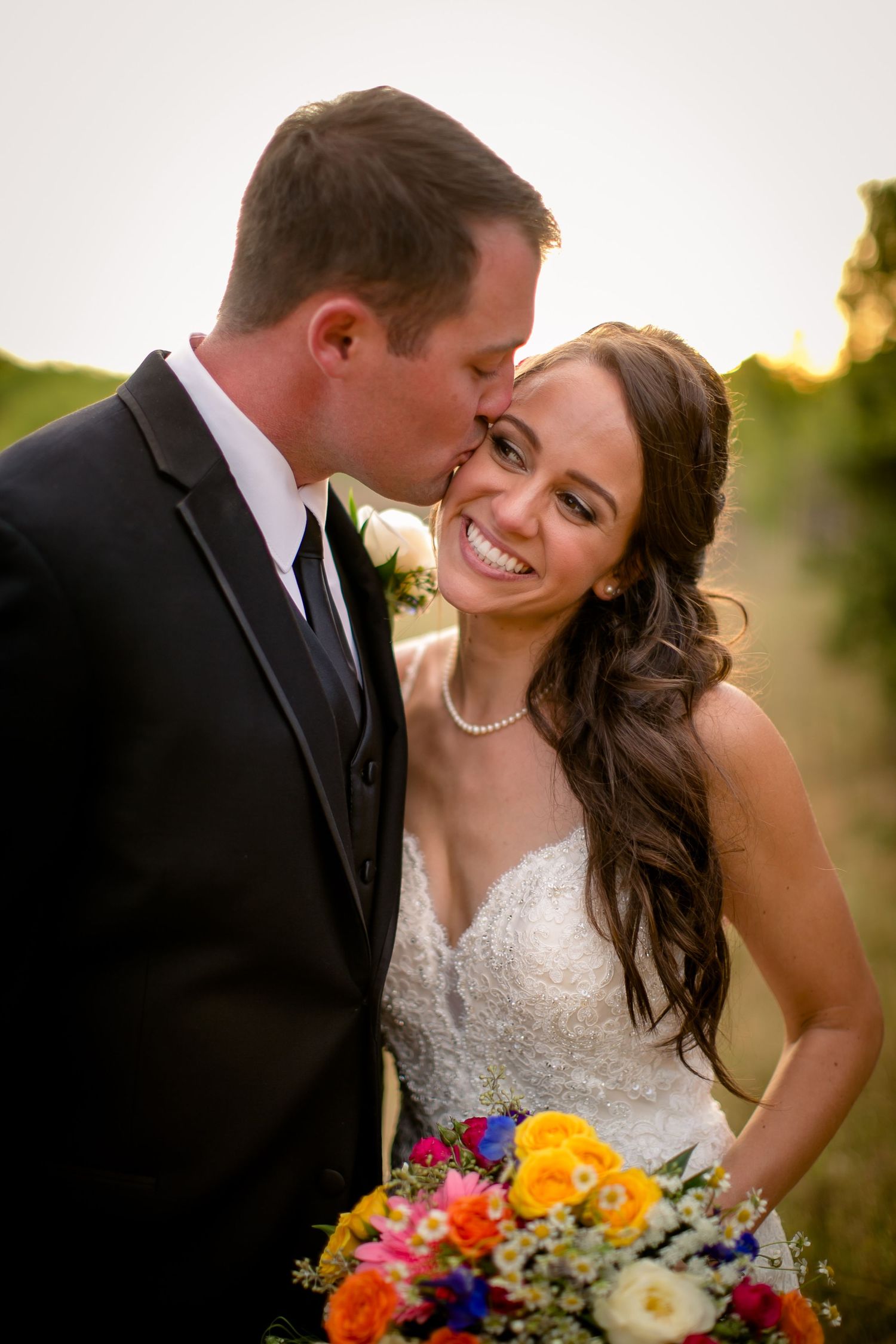 A romantic wedding moment captured outdoors with a colorful bouquet featuring yellow and pink flowers at sunset.