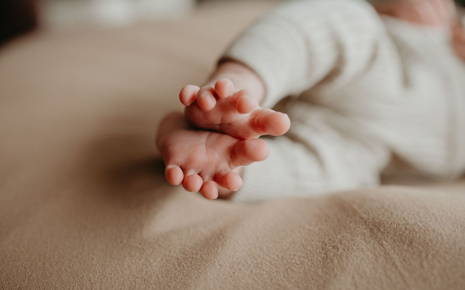 Close-up of tiny baby feet with pink toes resting on soft beige fabric.