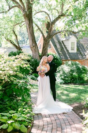 Bride and groom share a romantic kiss on a brick garden path surrounded by lush greenery and flowering shrubs.