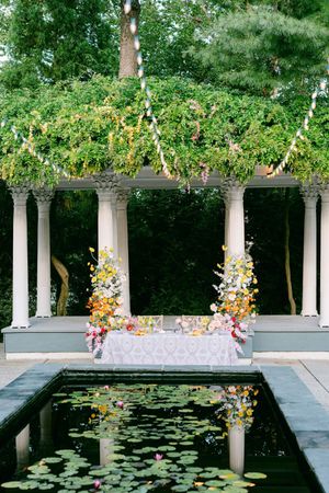 Elegant garden pool with lily pads surrounded by white columns and decorated with floral arrangements for an outdoor event.