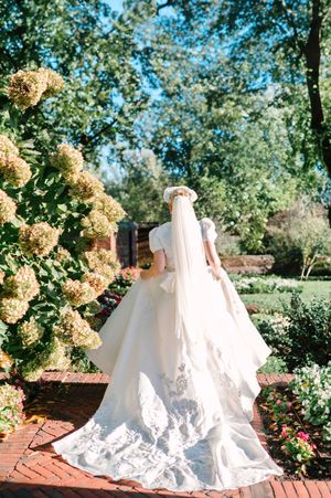 A flowing white wedding dress with long train photographed in a garden with blooming hydrangeas.