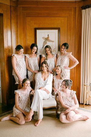 Wedding party lounging in matching blush robes against wood-paneled walls.