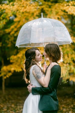 Couple sharing intimate moment under clear umbrella with autumn foliage in background.