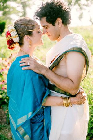 Couple embraces in turquoise and white wedding attire against a sunlit garden backdrop.