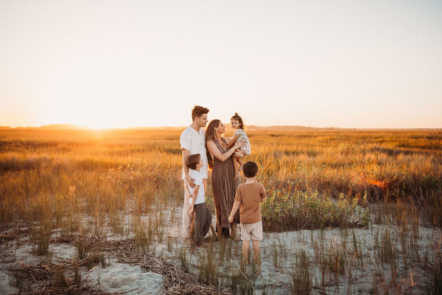 A romantic couple embraces in a golden field at sunset while their silhouettes are illuminated by warm sunlight.