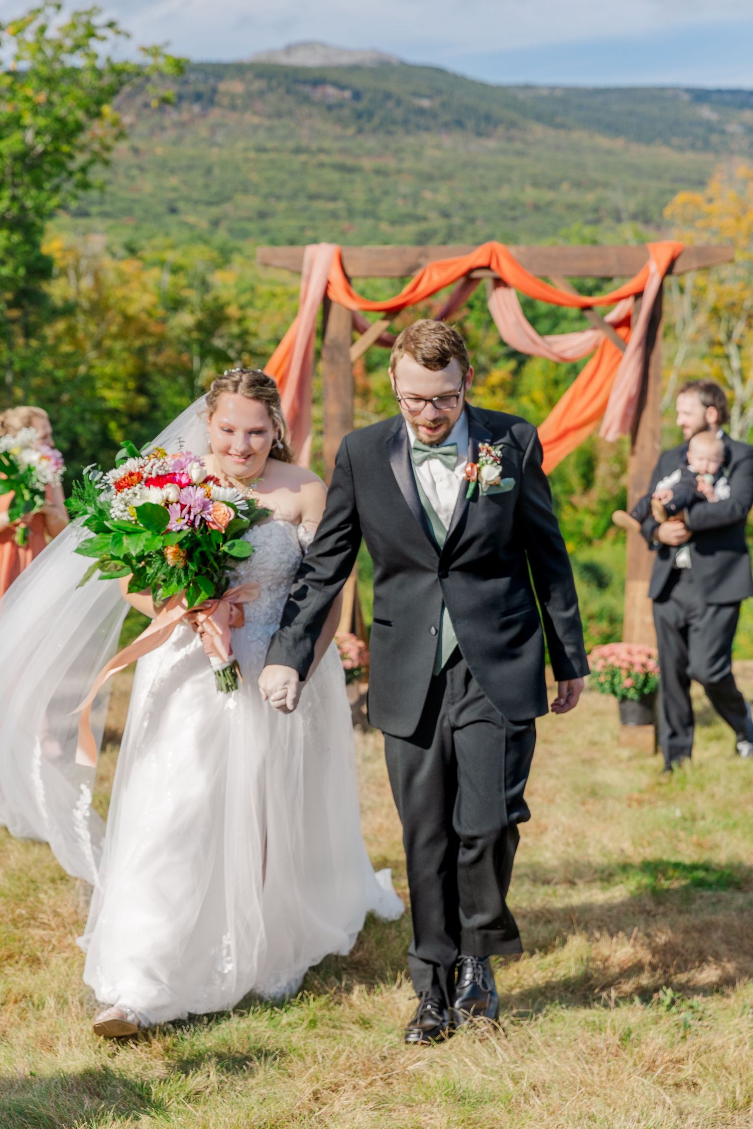 Newlyweds exit their mountain wedding ceremony under wooden arch with coral draping.