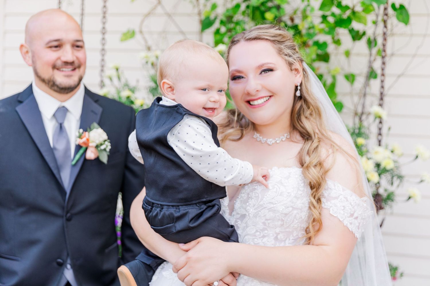 A wedding party poses with a small child in formal attire against a white wall.