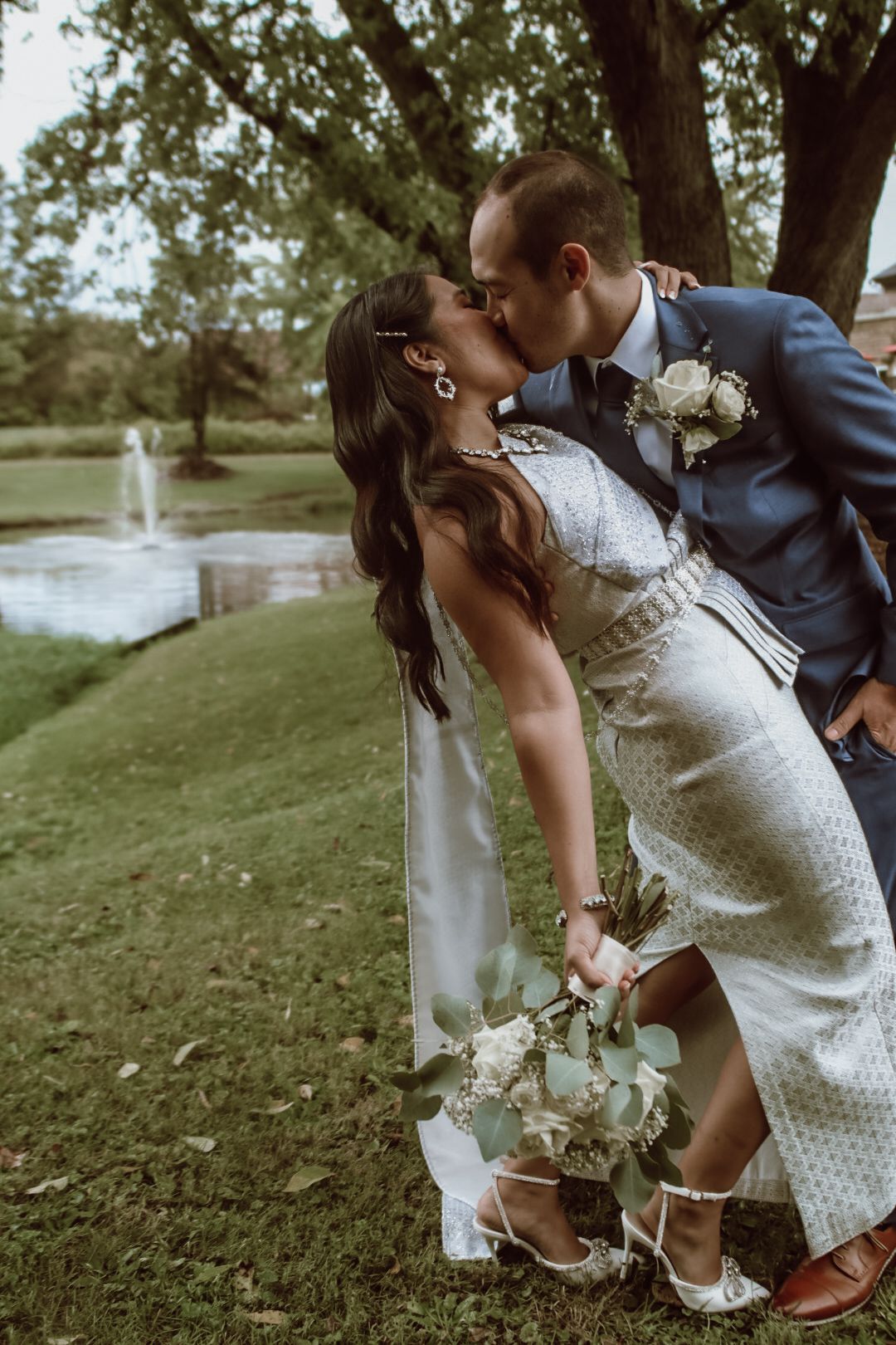 Romantic wedding couple shares intimate moment by fountain in garden setting.