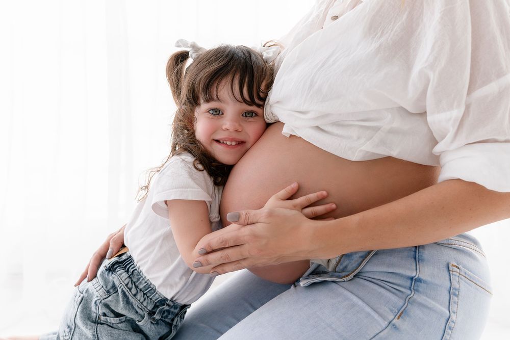 Tender moment captured of child embracing pregnant belly in casual setting.