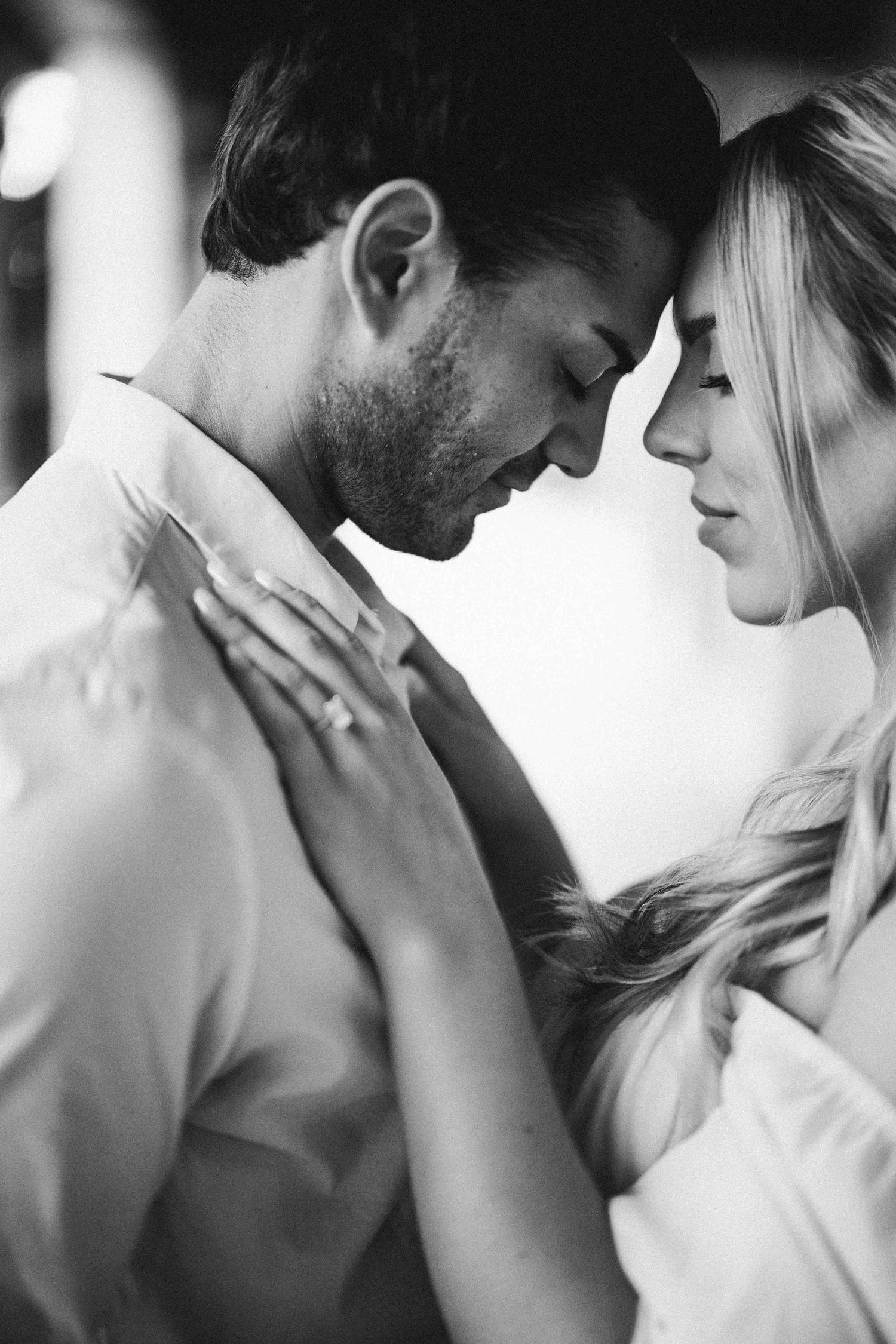 An intimate black and white portrait of a couple in a tender embrace.