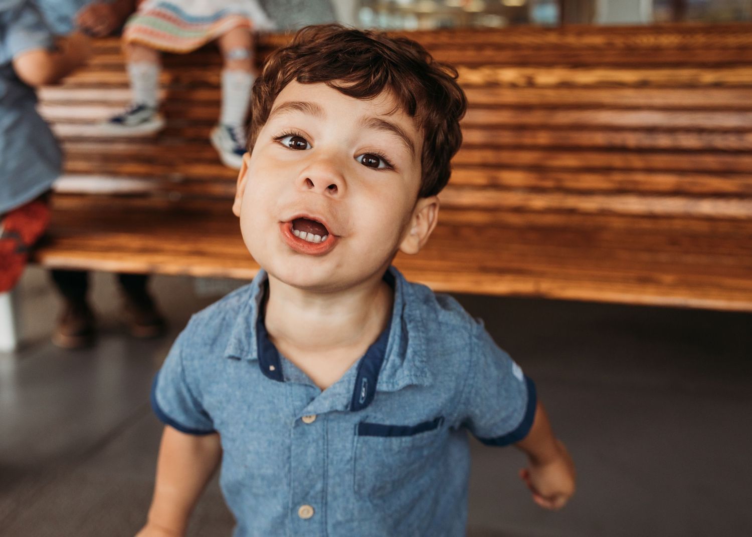 Young child in blue shirt smiling with excitement at the camera.