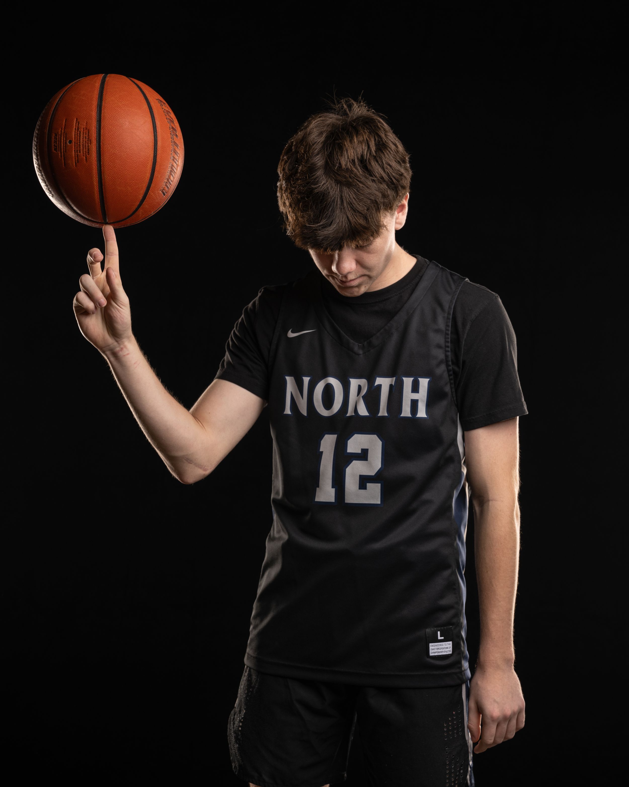 Basketball player in black North #12 jersey spinning ball on finger against dark background.