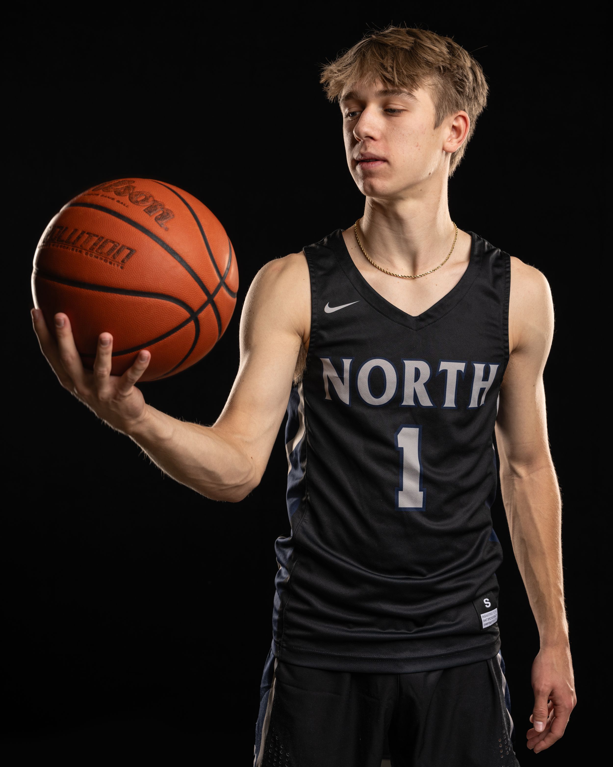 Basketball player wearing black North jersey number 1 poses holding a Wilson basketball against dark background.
