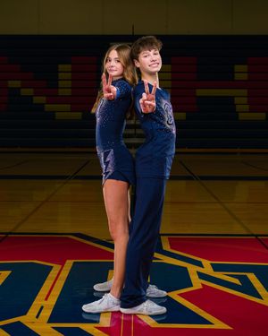 Two cheerleaders in blue uniforms pose together on a colorful gymnasium floor during a photo session.