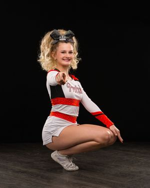 Smiling cheerleader in red and white uniform crouching in dynamic pose with sparkly bow hair accessory.