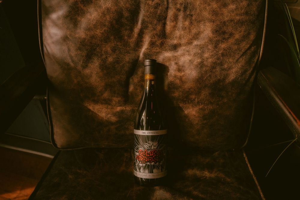 A single wine bottle with an artistic label resting on a worn brown leather chair in moody lighting.
