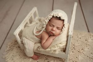 A sleeping newborn wearing a white knit hat rests peacefully on cream-colored lace bedding. – newborn photographer Paloma Schell Houston TX
