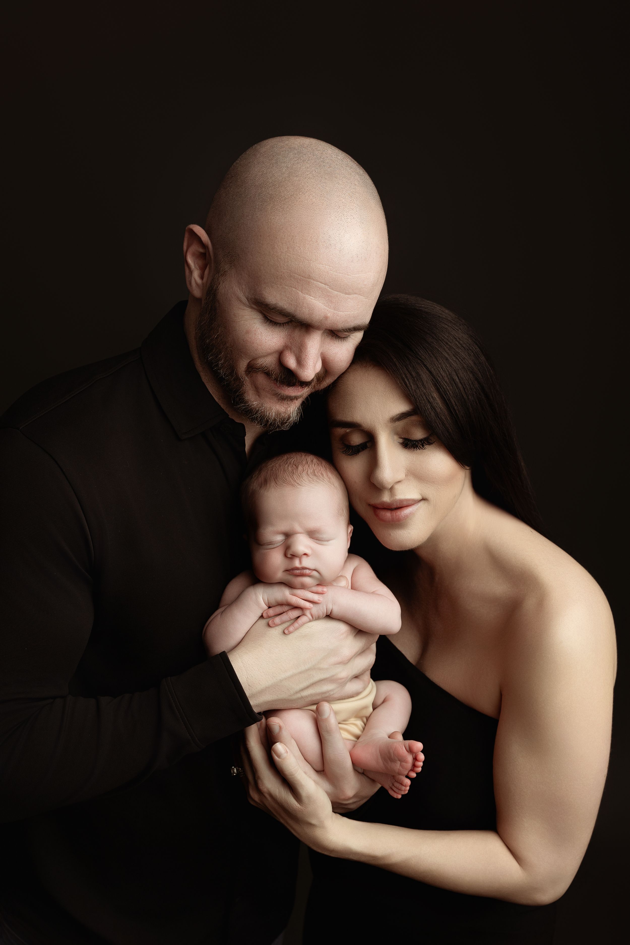 A family portrait in dark tones shows parents holding their sleeping newborn.