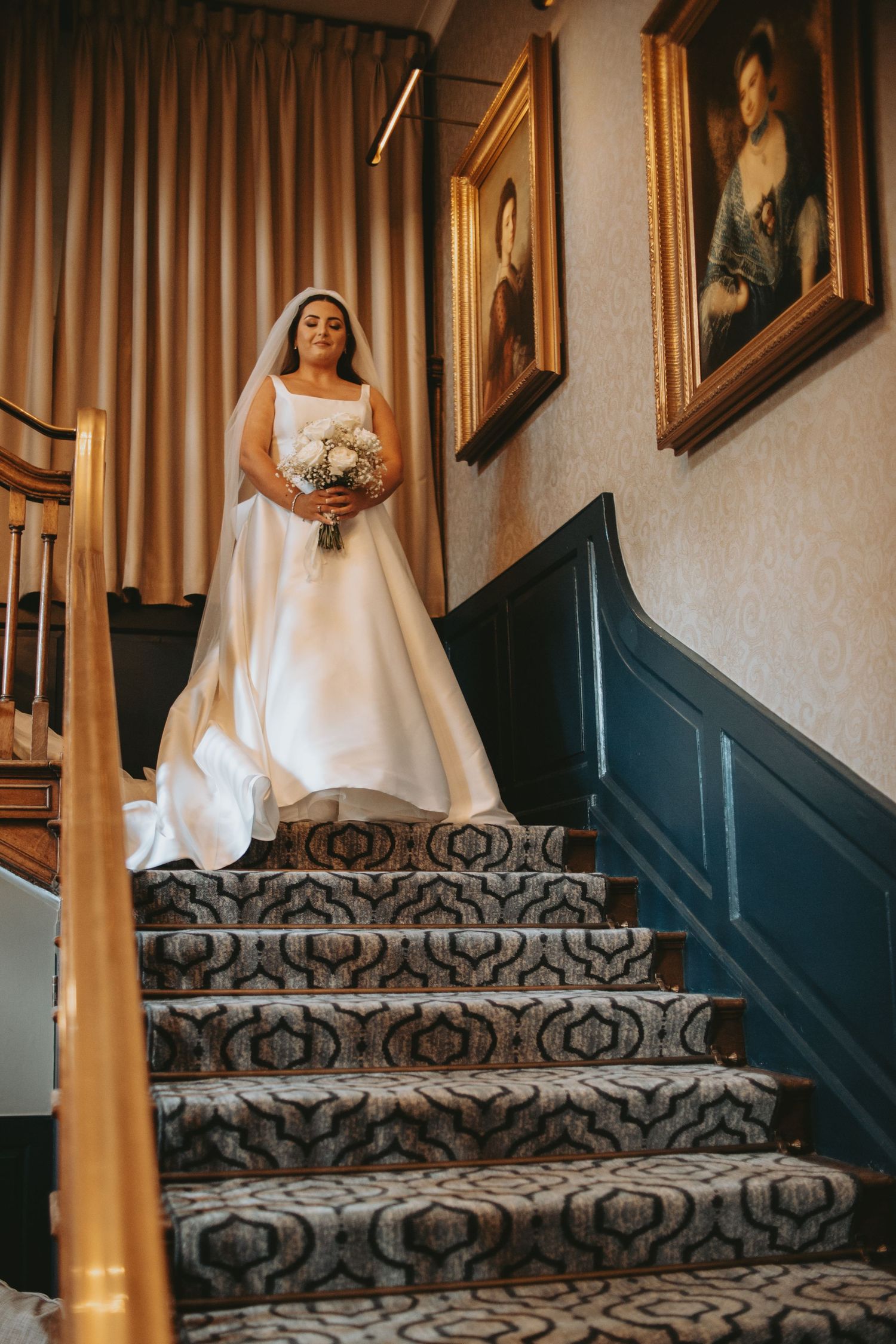 Elegant bride descending patterned carpeted stairs in a flowing white wedding gown.