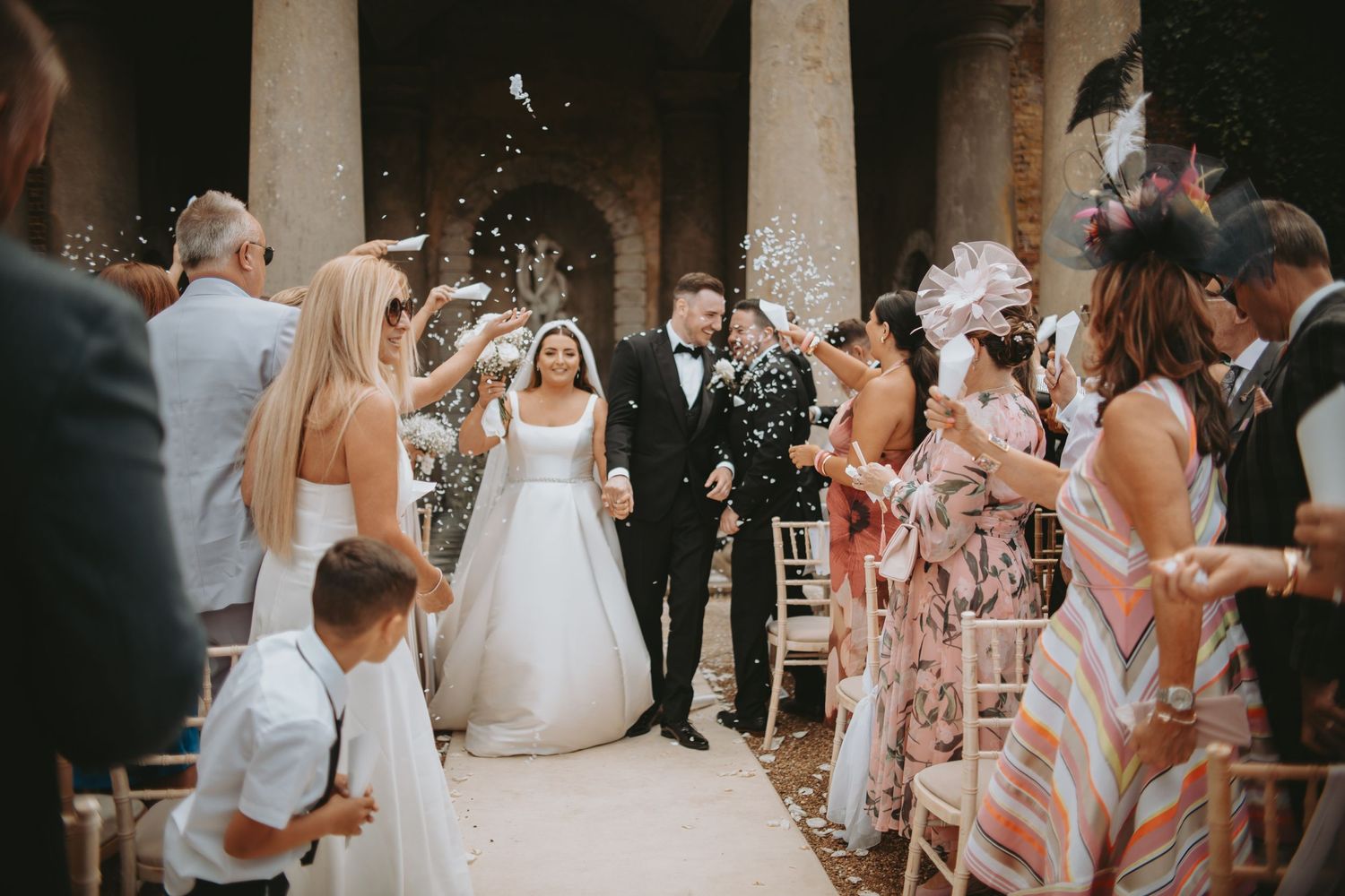 Joyful wedding exit with guests throwing confetti in outdoor garden setting.