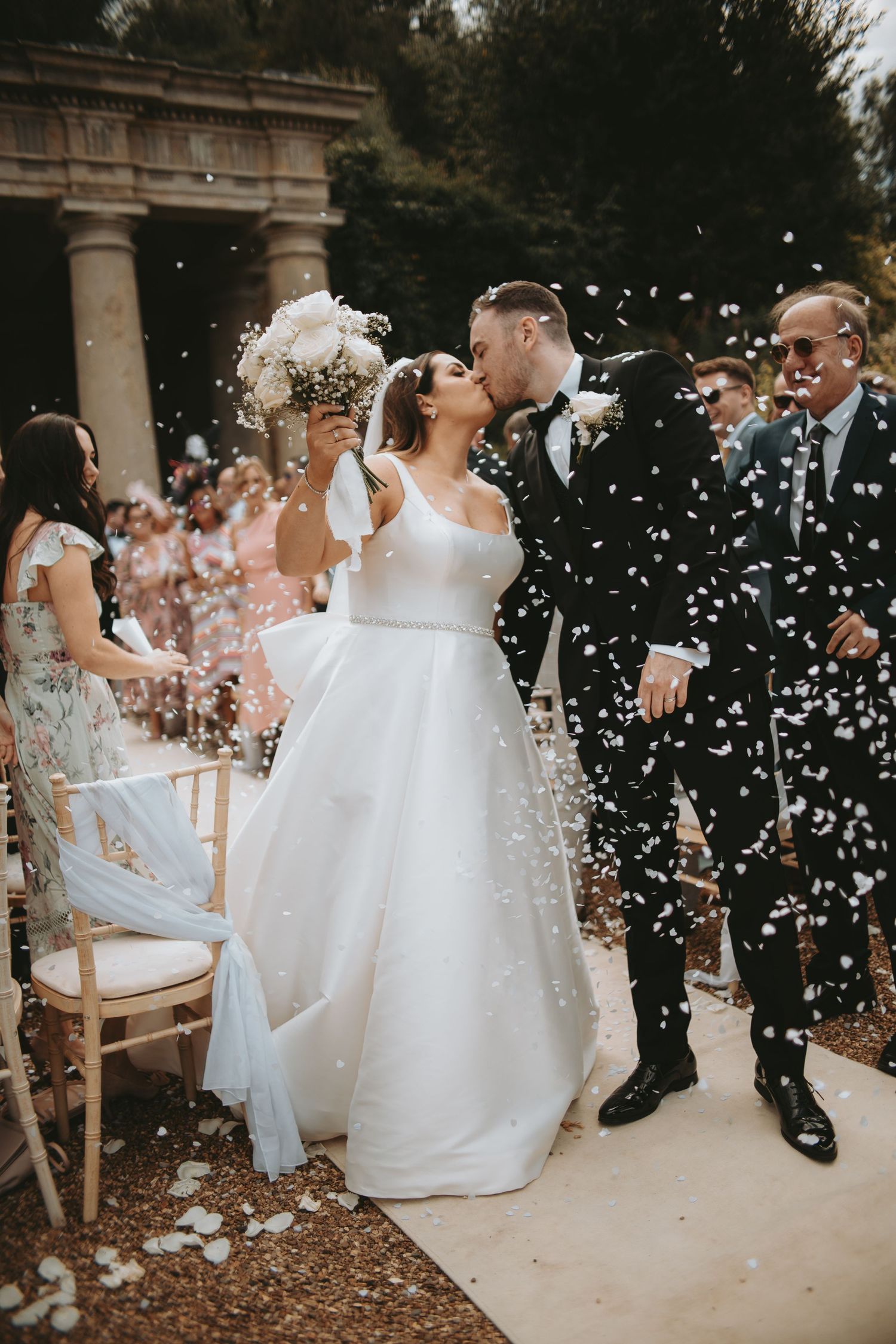 Romantic wedding moment captured with confetti shower in garden setting.
