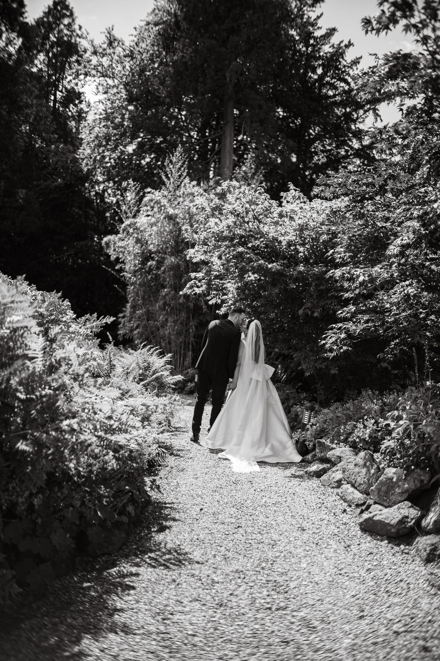 Monochrome image of couple strolling through tree-lined garden pathway.