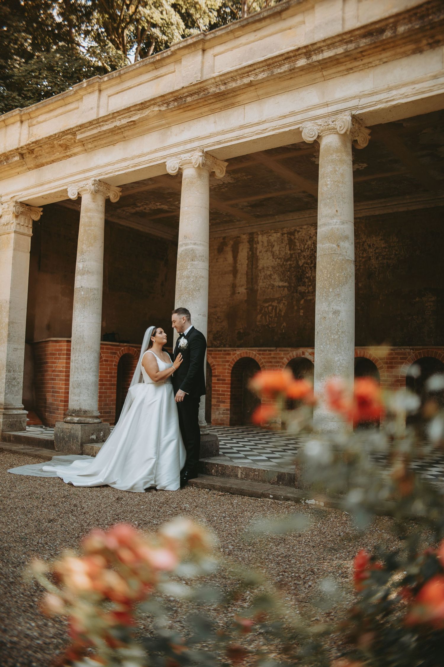 Wedding couple poses in front of a classical columned portico with brick and stone architecture.