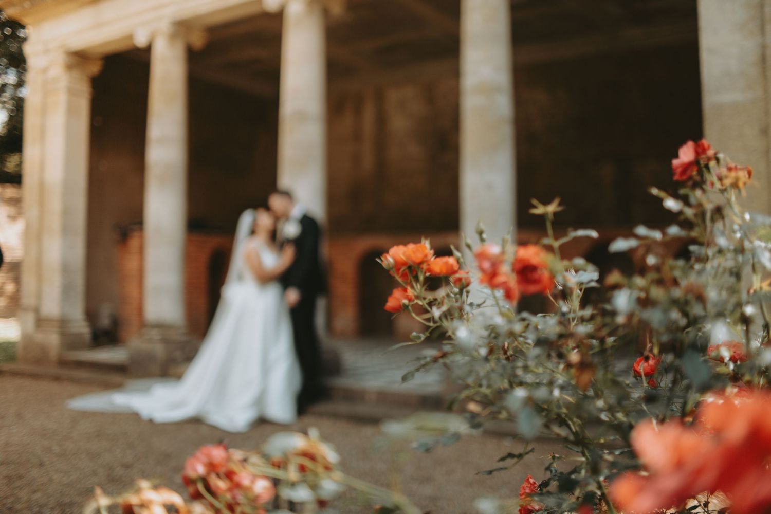 Elegant wedding scene with couple standing beneath historic stone colonnade at sunset.