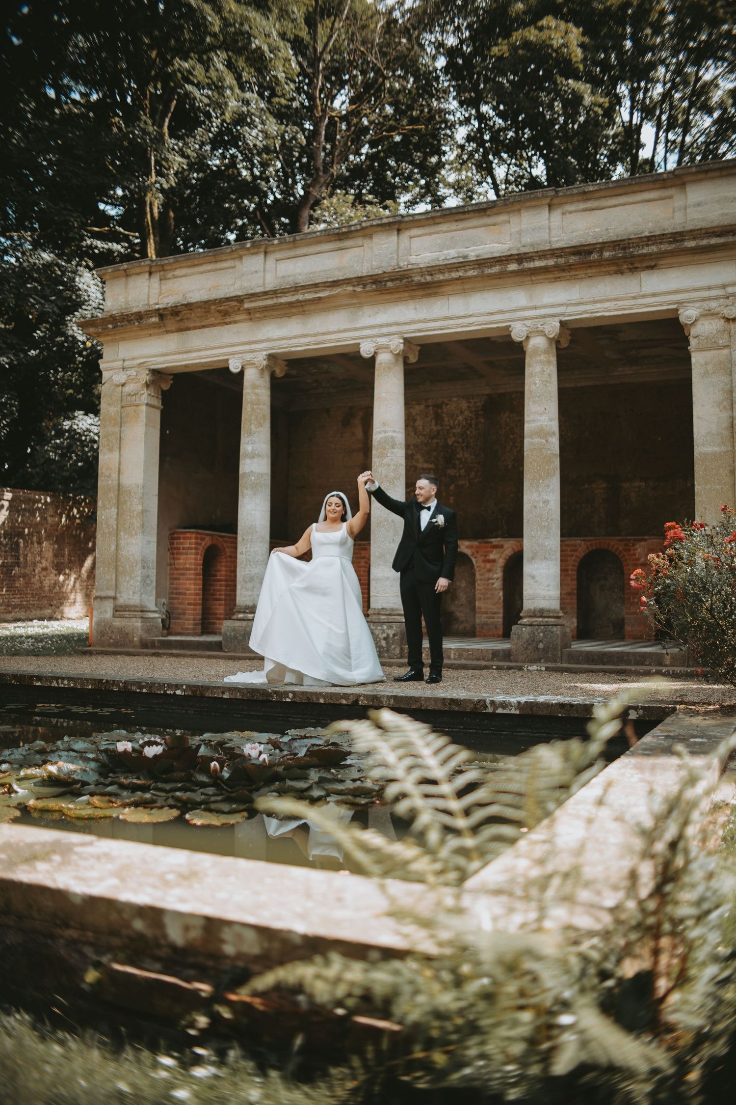 Romantic wedding photo captured at historic venue with stone columns and autumn foliage.