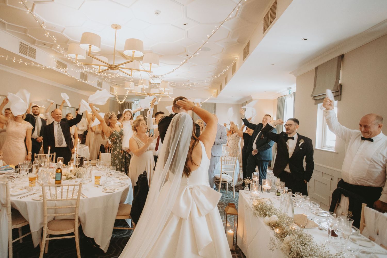 Wedding reception celebration with guests dancing under elegant chandeliers.