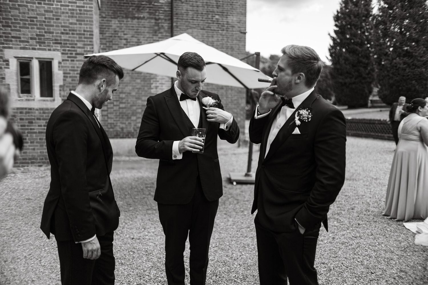 Wedding party members in formal attire socialize on a brick patio during an outdoor reception.