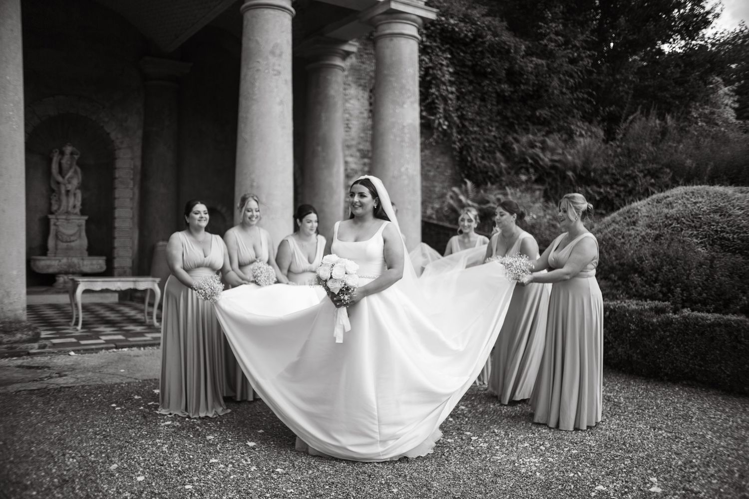 Wedding party poses under classical white columns during formal photography session.