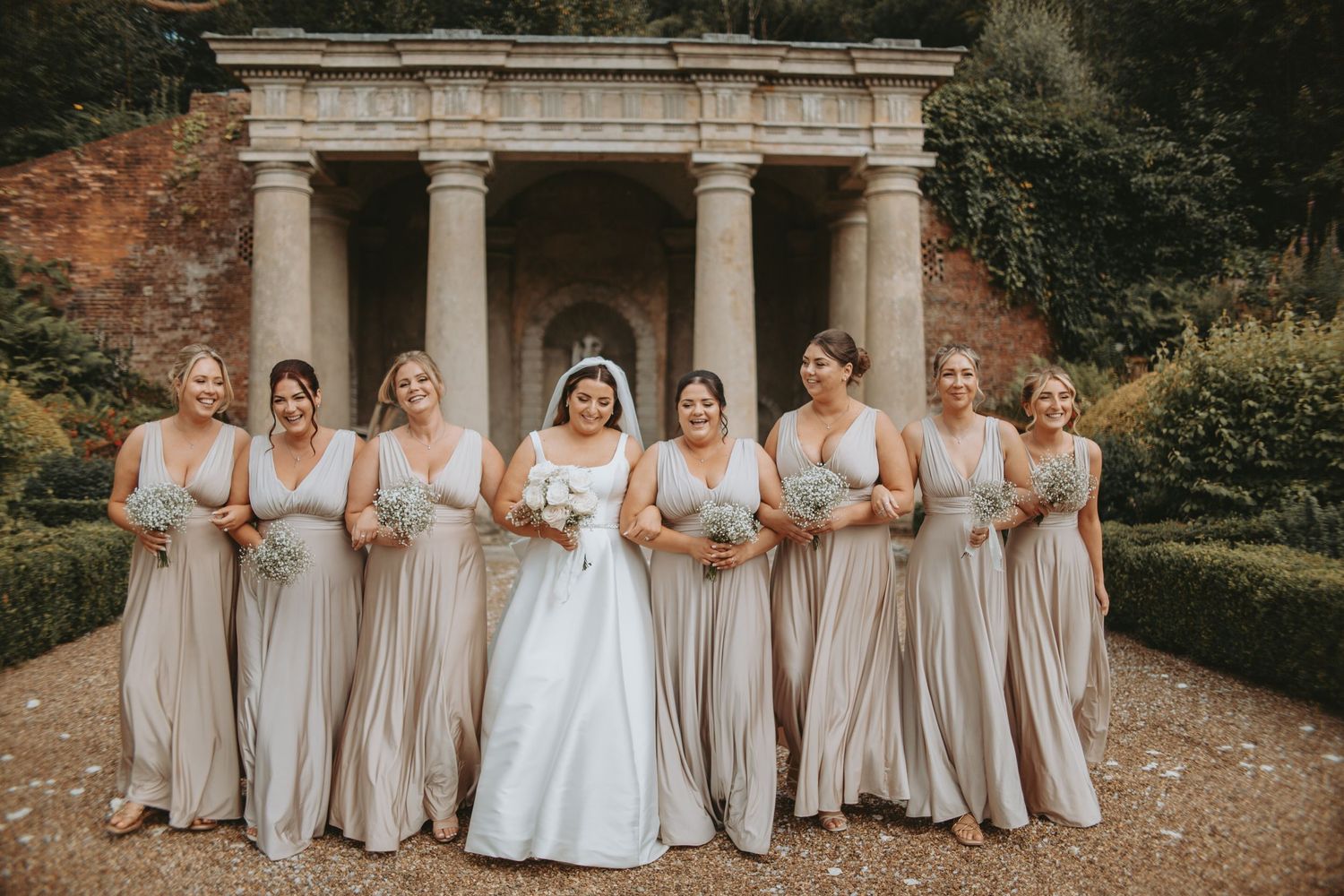 Bridesmaids in champagne dresses flank bride in white gown at elegant stone venue.