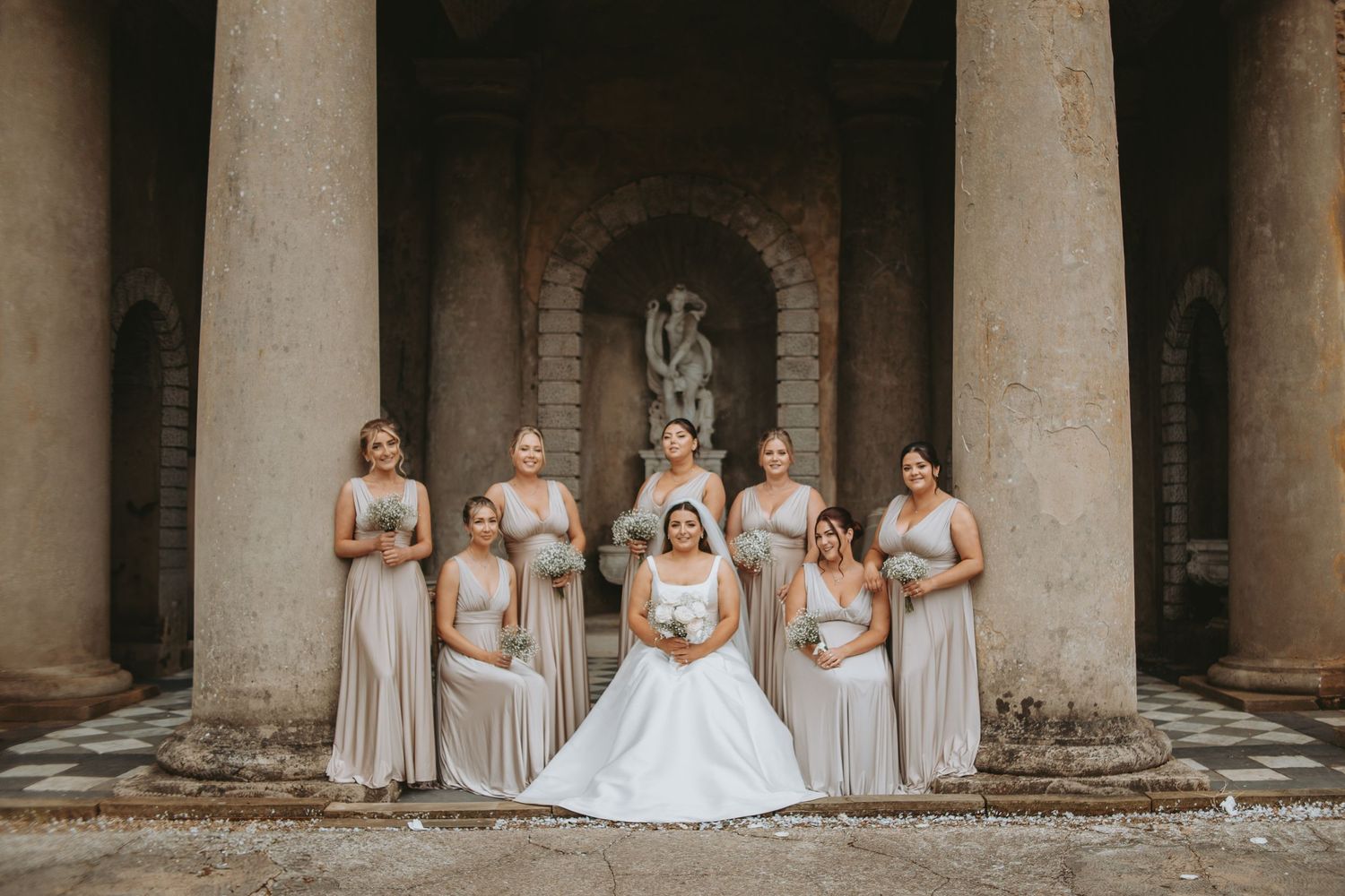 Artistic wide shot of wedding party posed in symmetrical stone archway.
