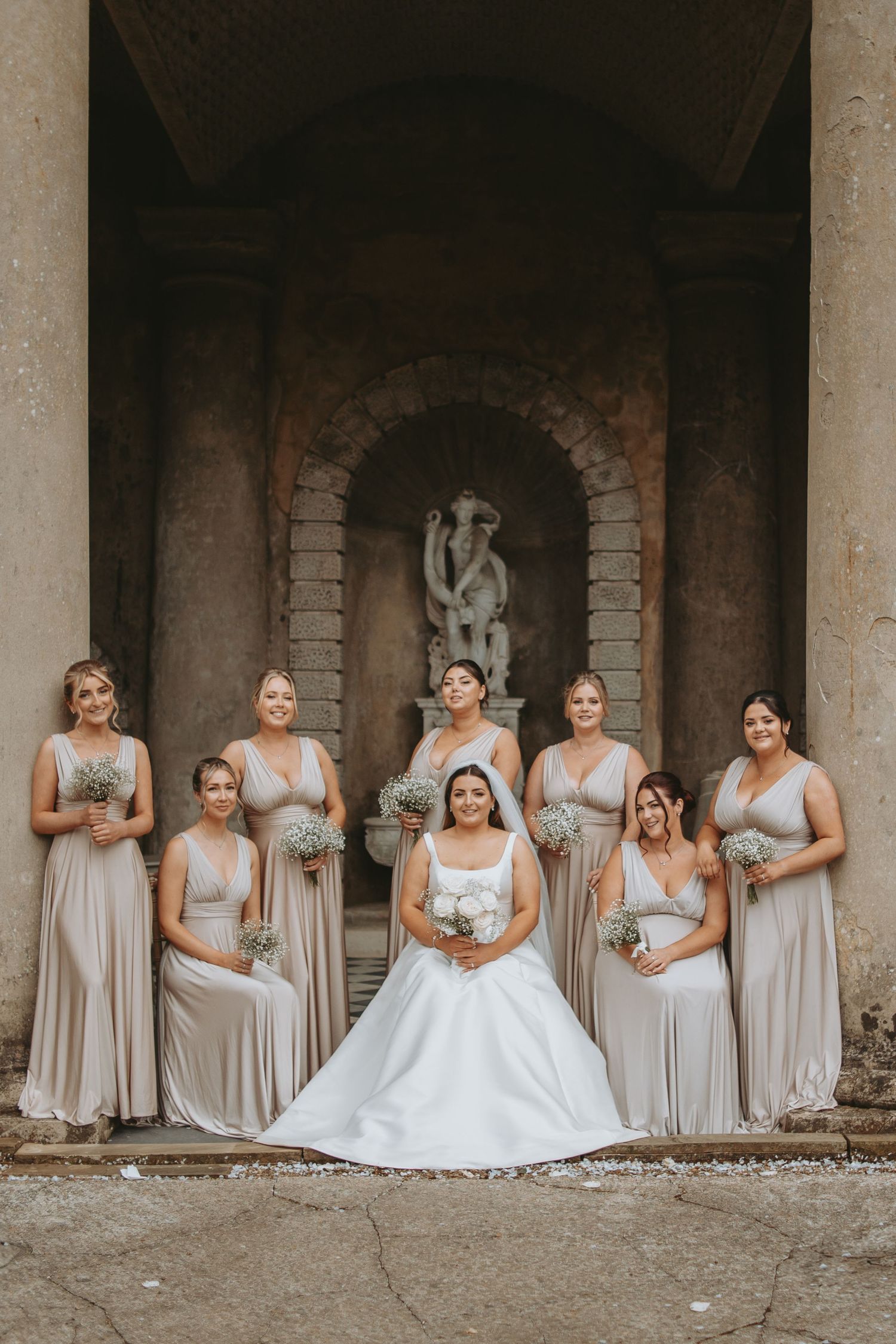 Wedding party arranged in elegant stone archway with bride in center wearing flowing white gown.