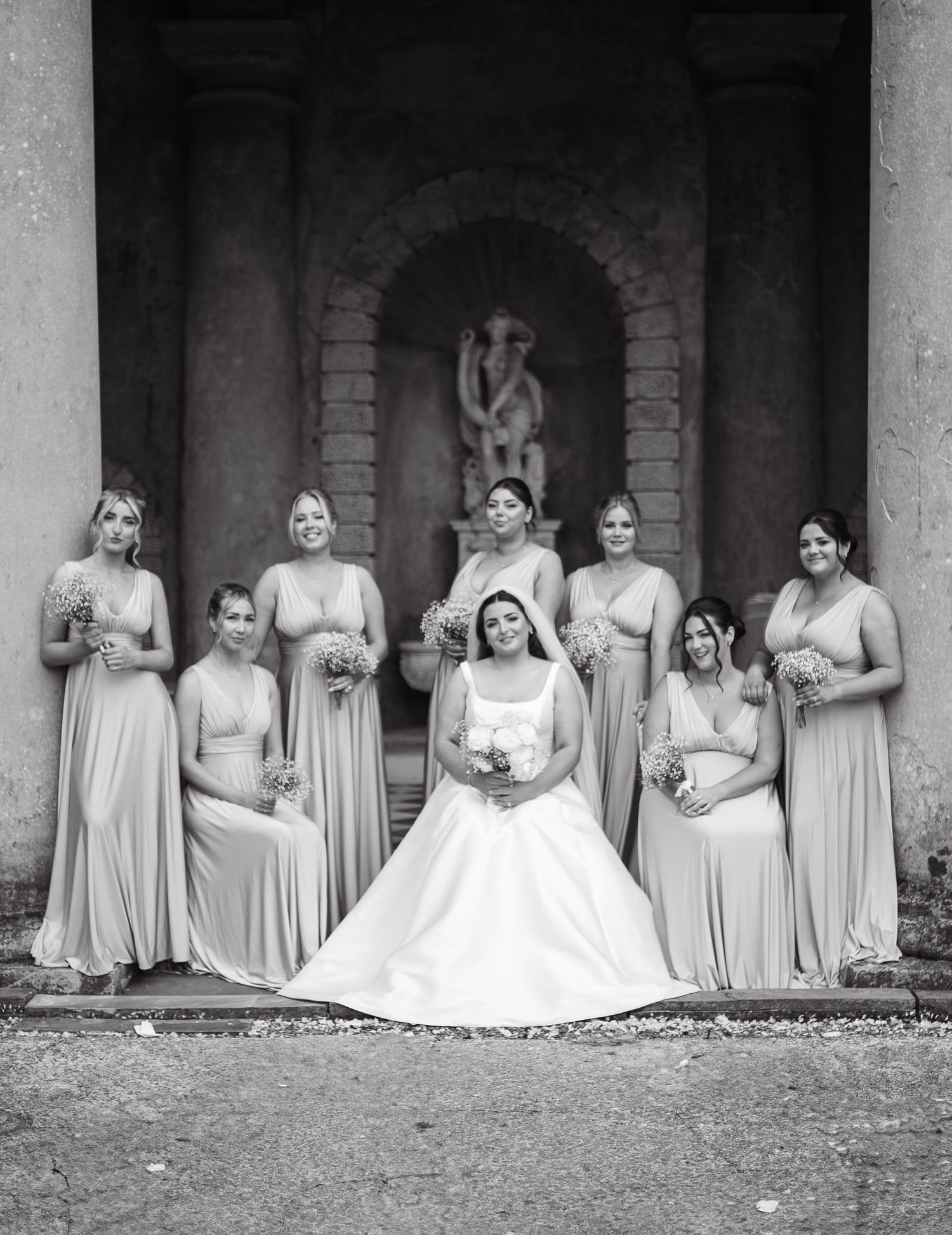 Black and white photo of bridal party seated in classical stone colonnade.