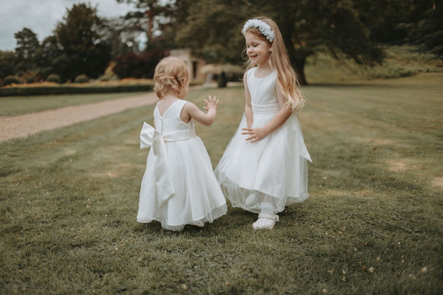 Two small figures in white dresses and shoes playing together on a grassy lawn.
