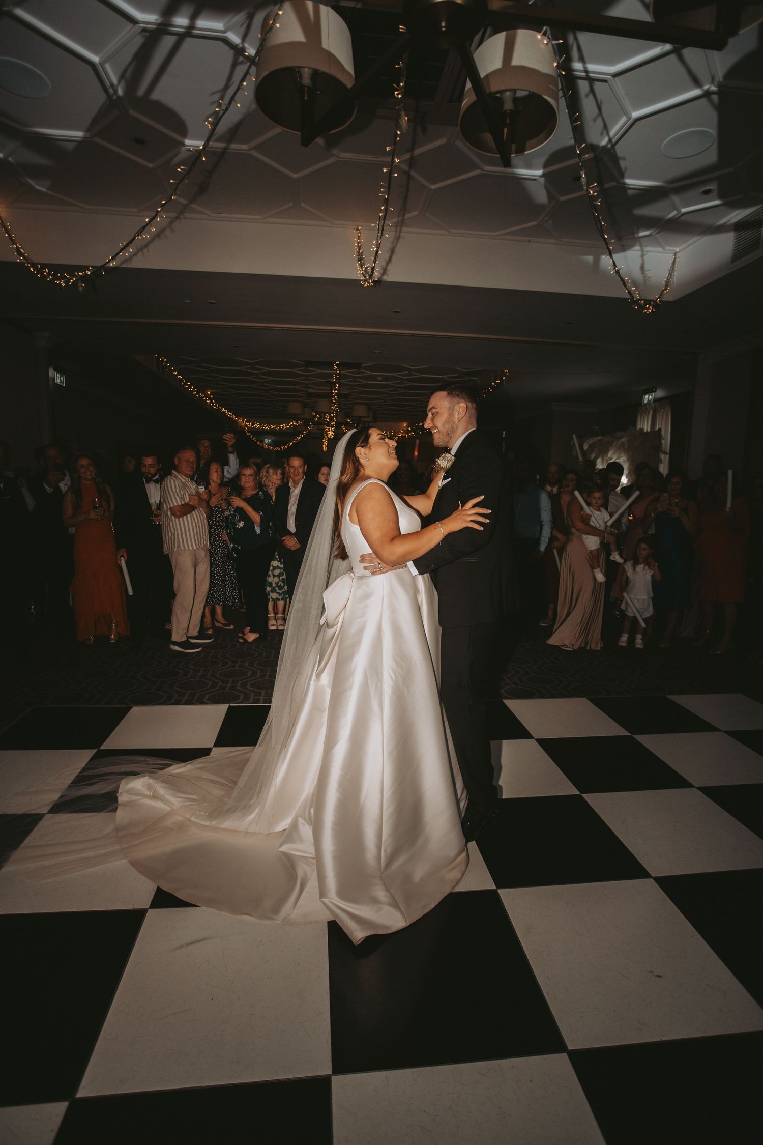 Wedding reception features dancing on black and white checkered floor under ambient lighting.