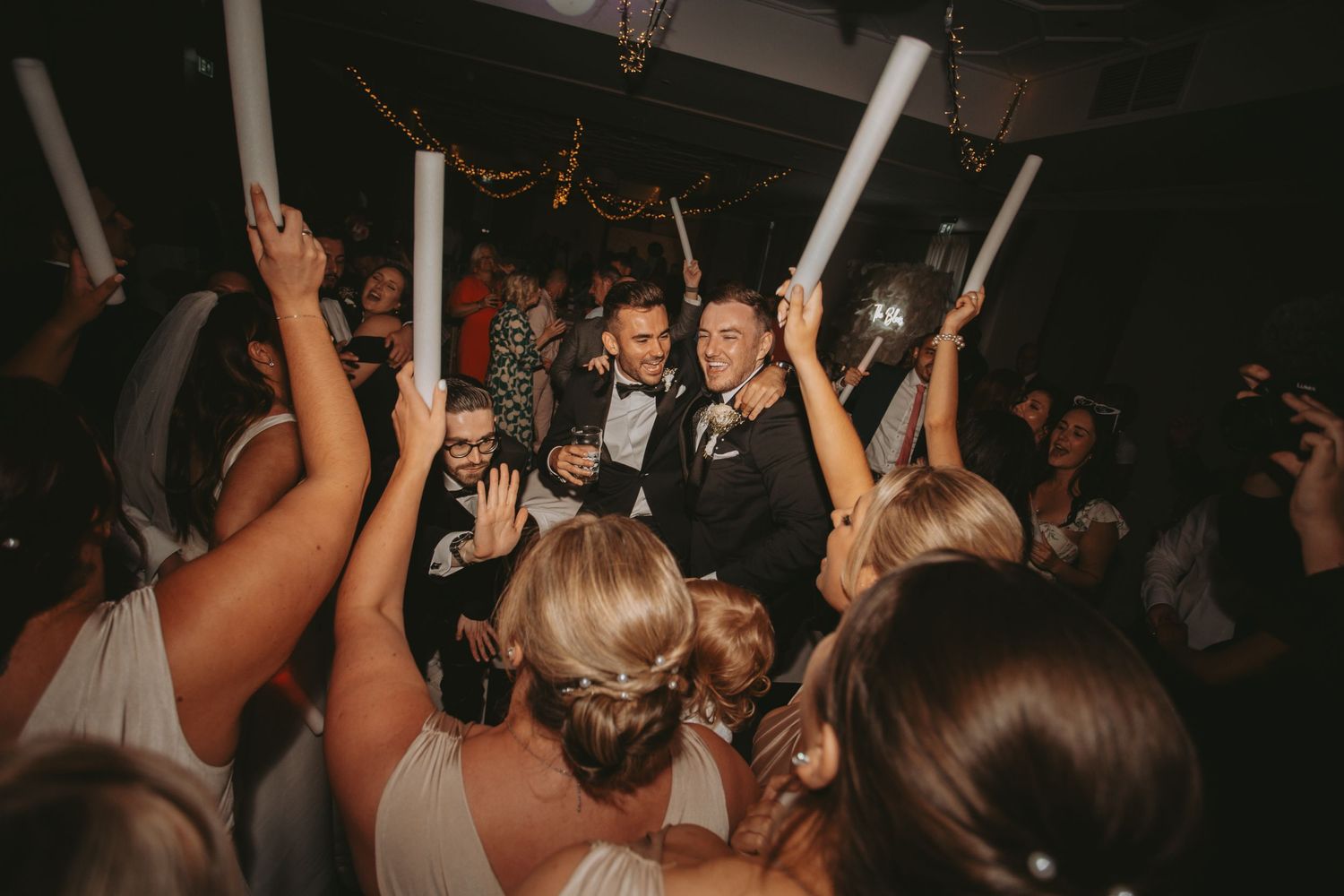 Lively dance floor celebration with guests holding glow sticks at wedding reception.