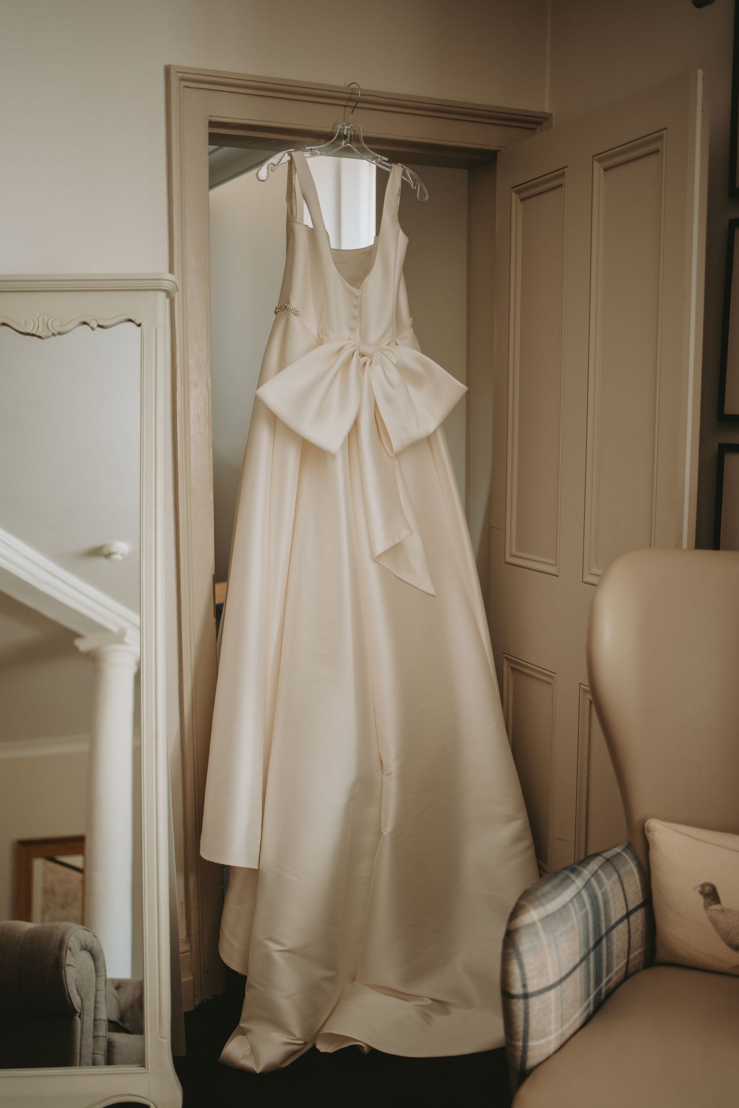 White wedding attire hanging in preparation room with natural lighting.