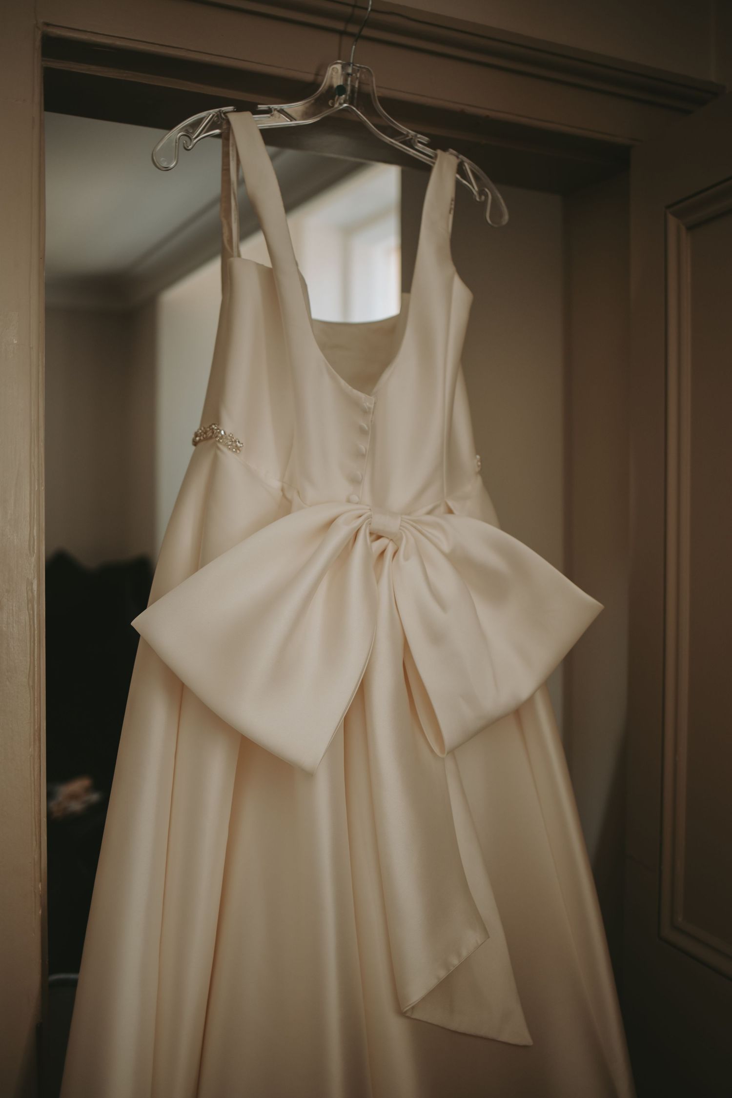 An elegant white wedding dress with a dramatic bow detail hangs on display.