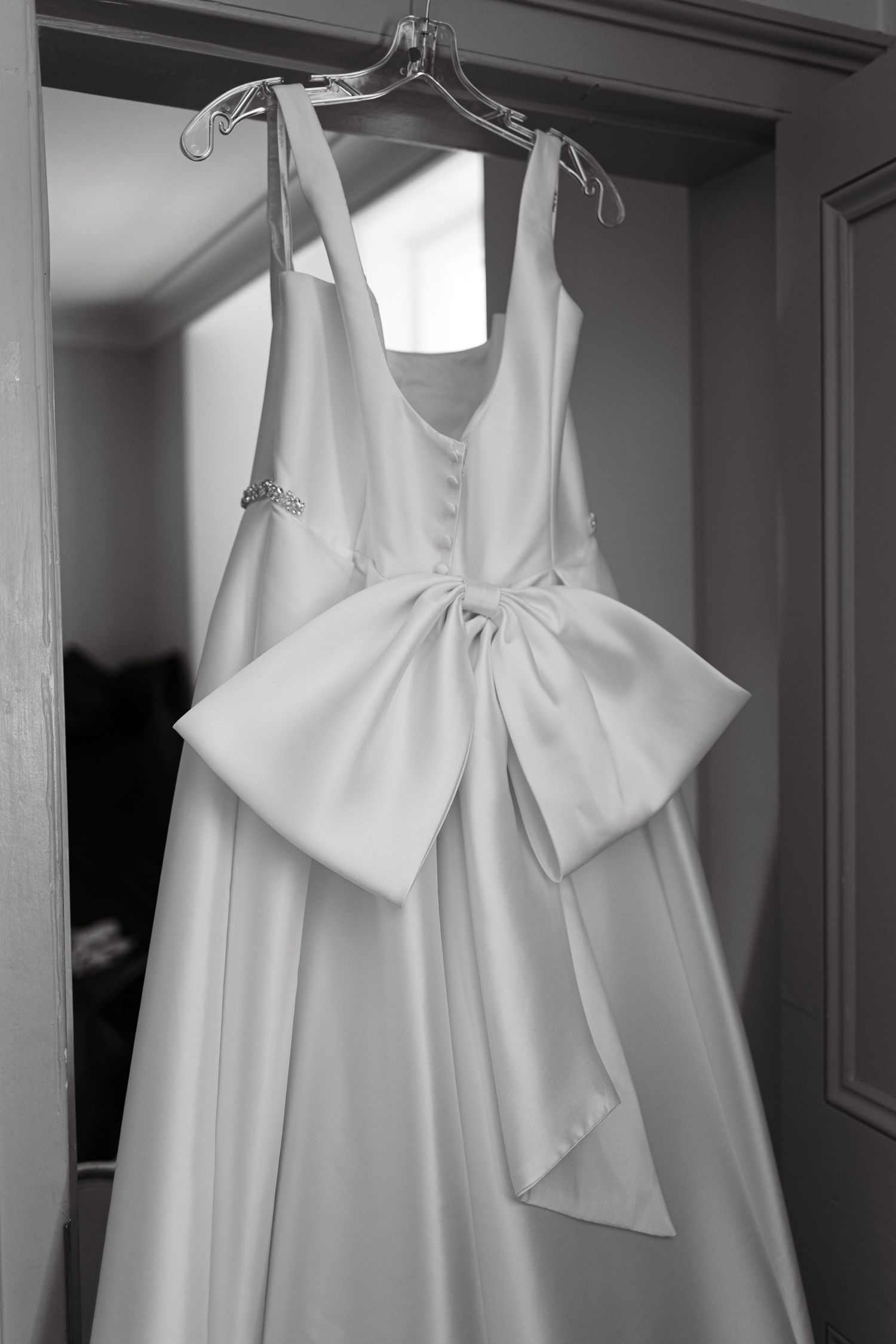 White wedding dresses with bow details displayed on hangers in dressing room.
