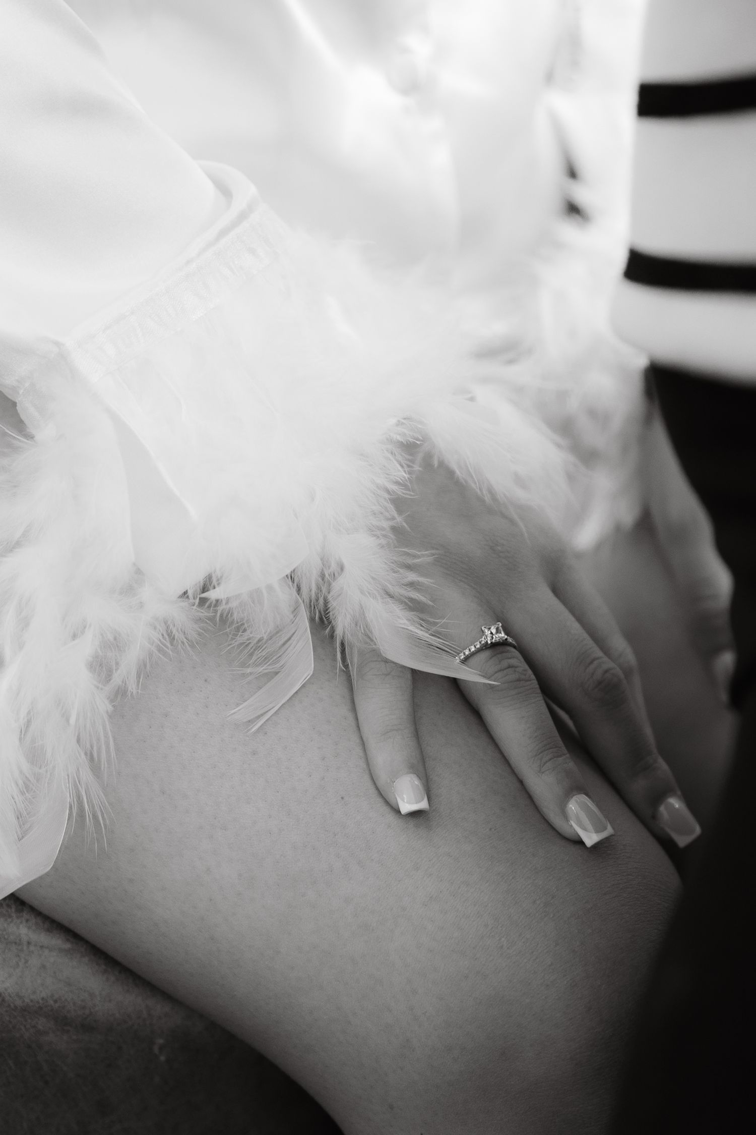 Close-up artistic black and white photo of hands with white feathers creating a delicate ethereal mood.