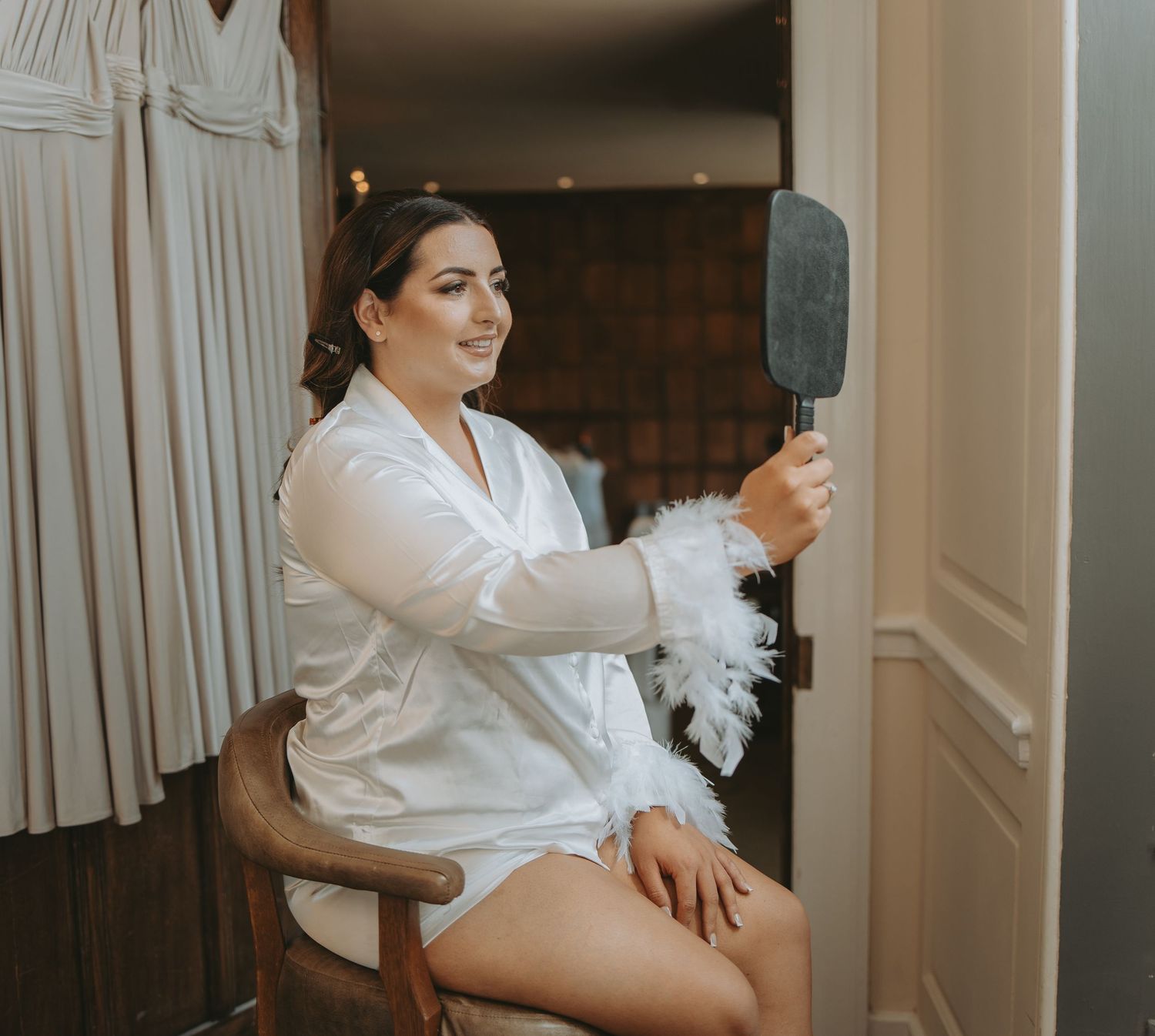 Wedding preparation scene with white robes and feather accessories in an elegant room.