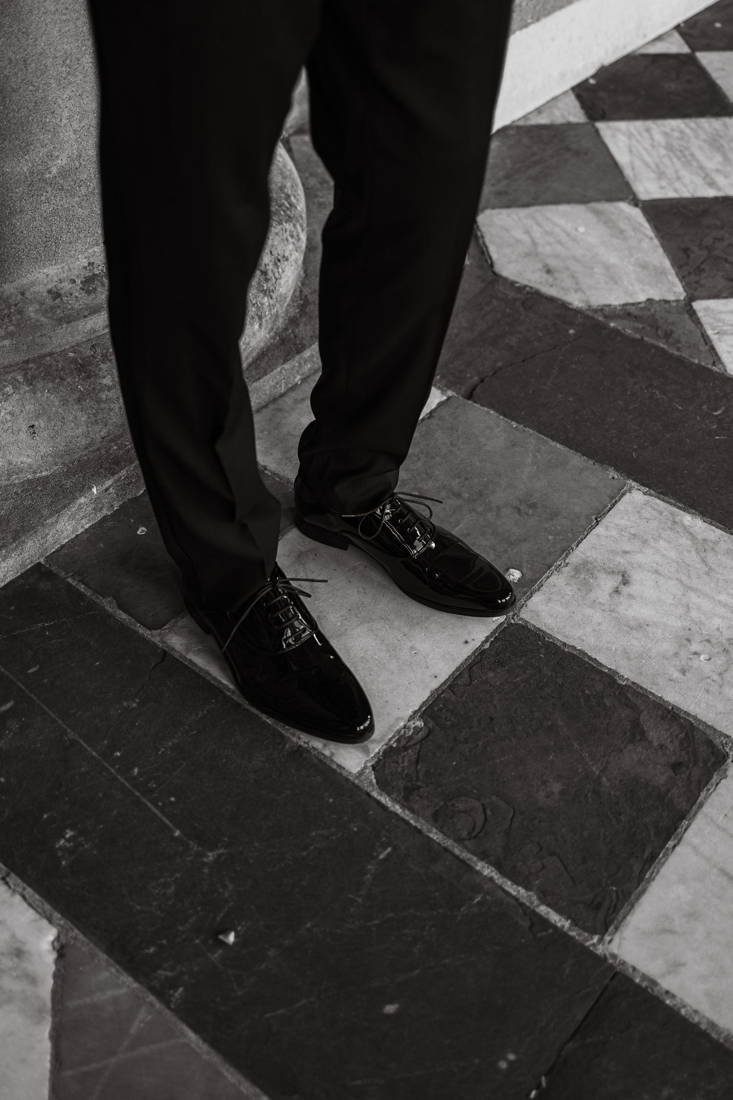 Close-up of polished black formal shoes on a checkered floor.