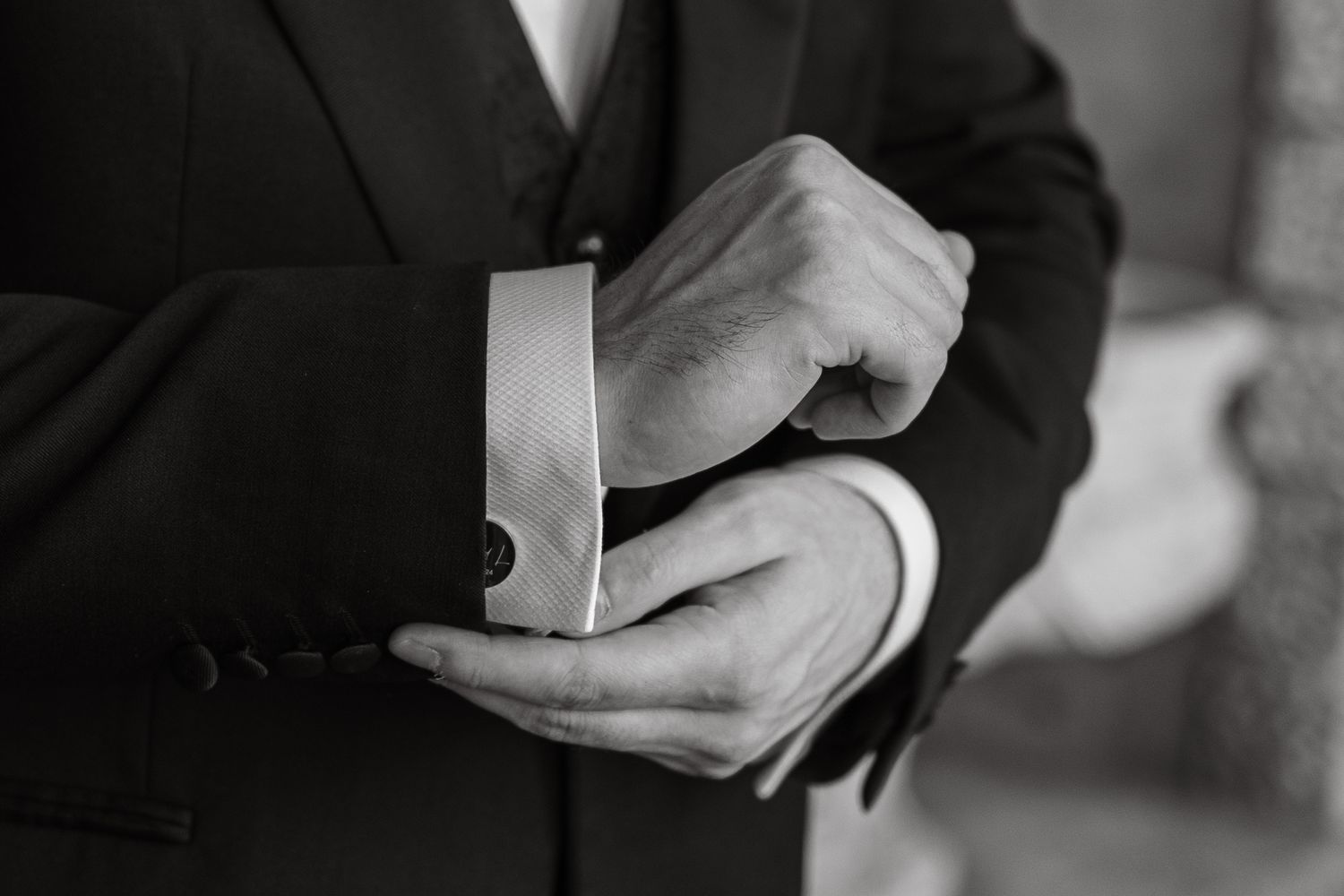 Close-up of hands adjusting formal shirt cuffs in black and white.
