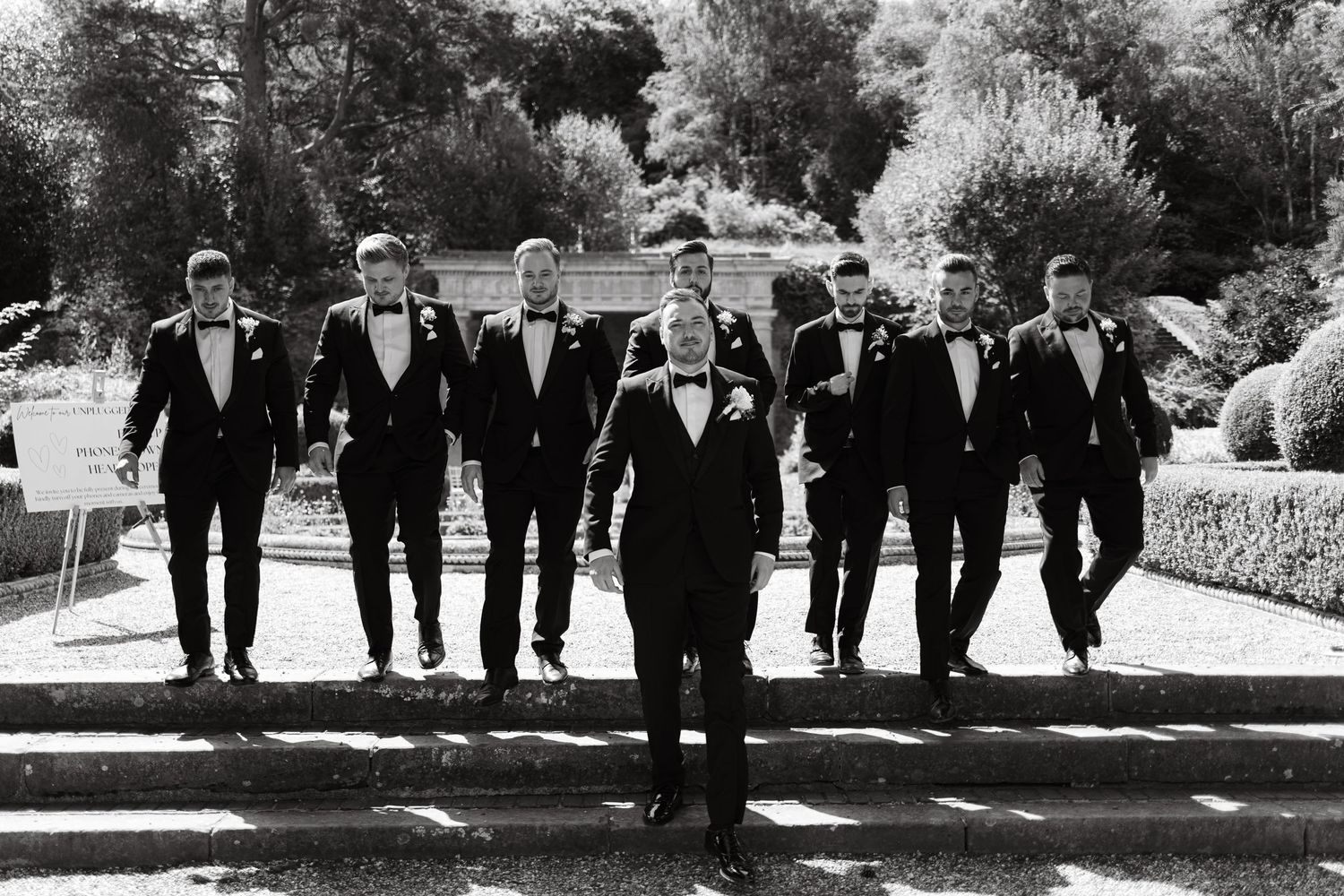 Wedding party walking together outdoors in formal black attire on a sunny day.